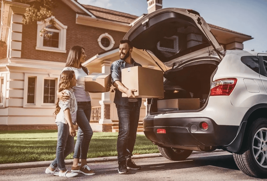 A man and two women loading boxes into the back of a car.