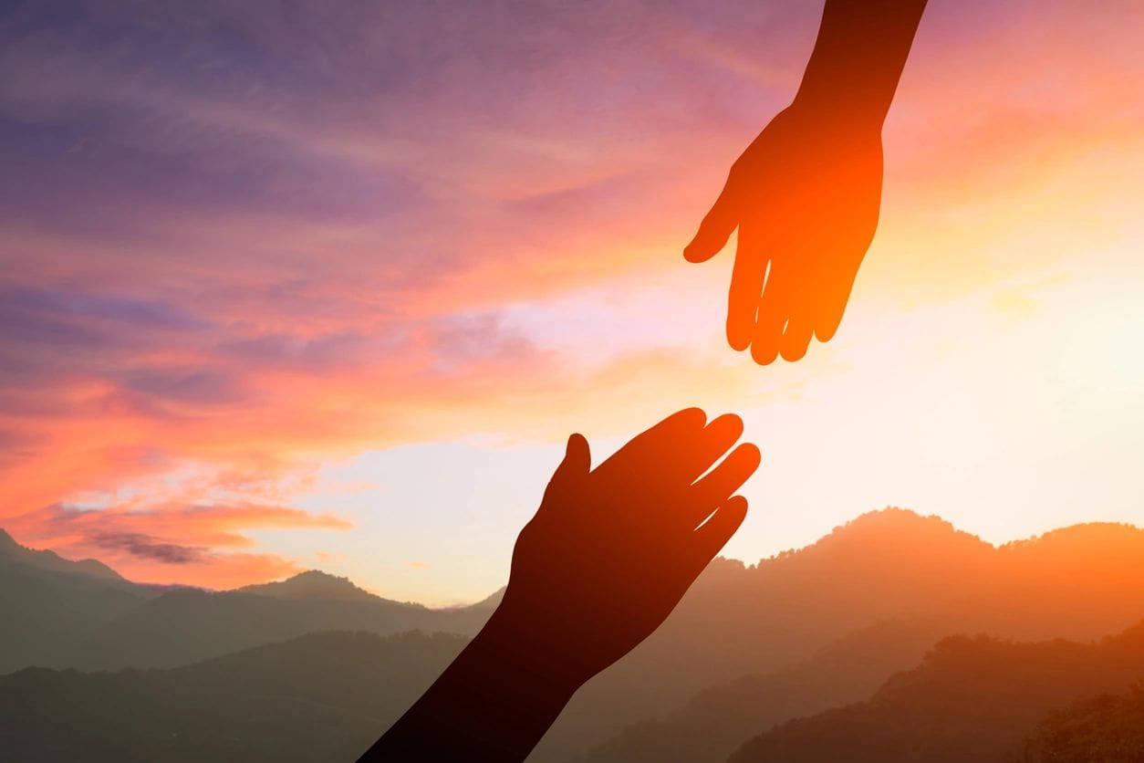 Two hands reaching out towards each other in the sunset.