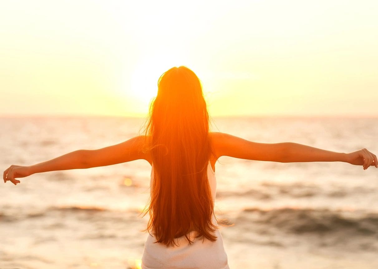 A woman standing on the beach with her arms outstretched.