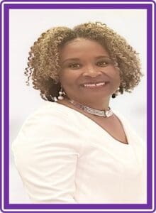 A woman with curly hair wearing white shirt and purple necklace.